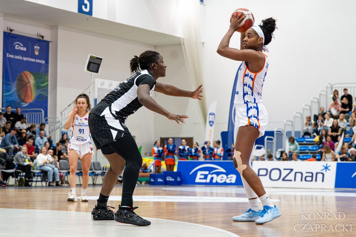 Zawodniczka Enea AZS w białym stroju z piłką uniesioną nad głową, kryta przez koszykarkę Landerneau Bretagne Basket; w tle Malina Piasecka (nr 91) i kibice w hali CSPP