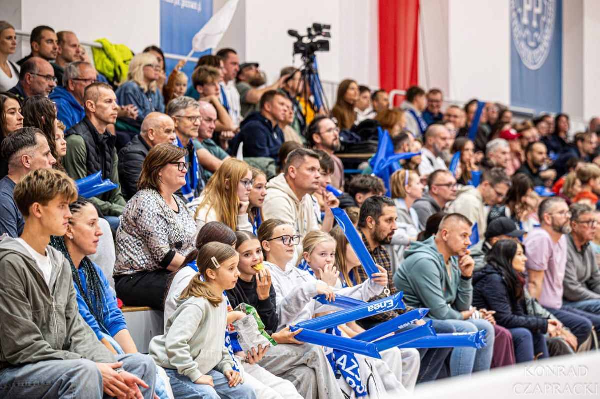 Kibice na trybunie hali CSPP, wśród nich dzieci, z niebieskimi dmuchanymi kijkami do kibicowania.
