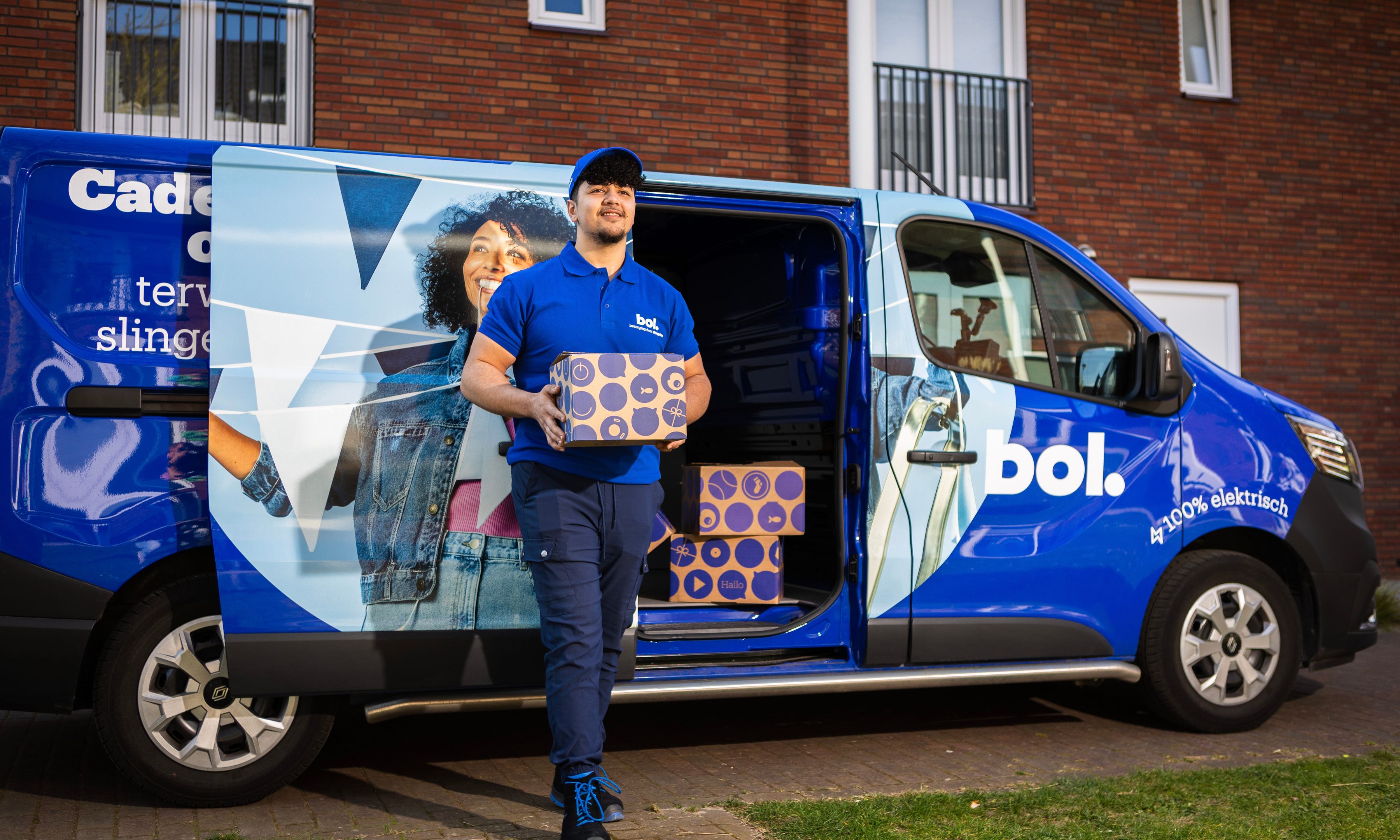 Bol chauffeur met een pakketje in zijn hand, op de achtergrond een bol-busje.
