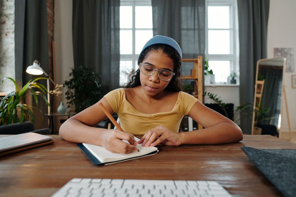 A young teen writing in a notebook at a wooden desk