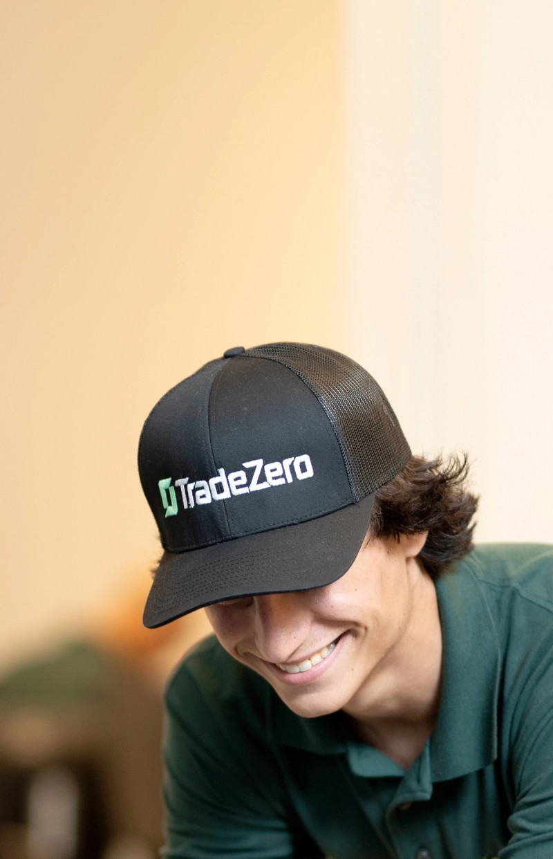 Young men wearing TradeZero merch smiling while looking at a computer screen