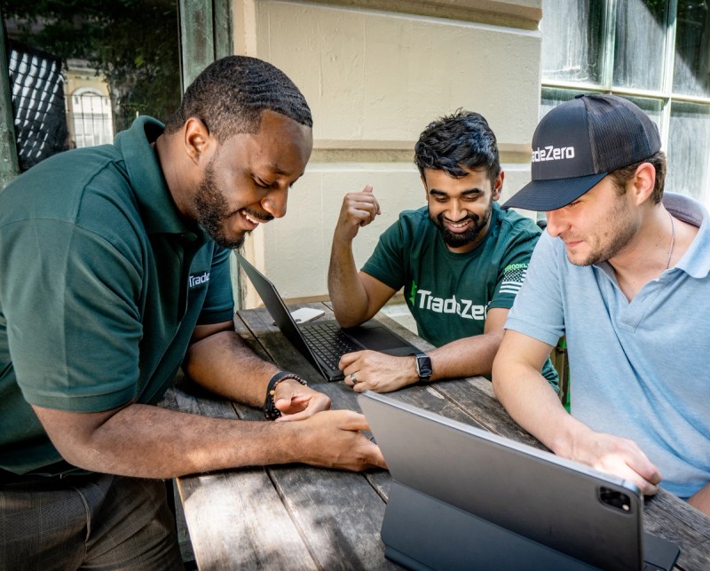 Three guys trading outdoors with a computer, a tablet and a phone wearing TradeZero custom merch