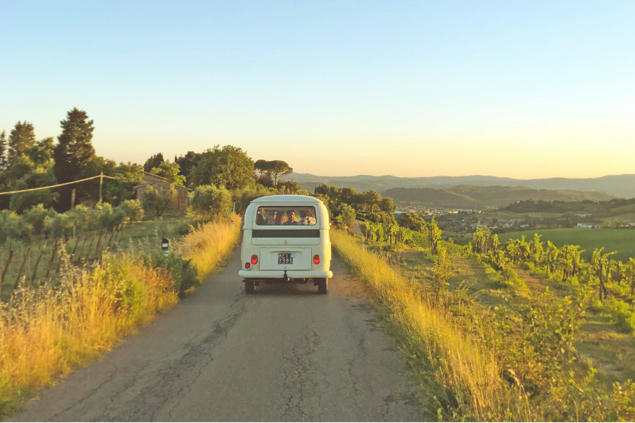 A van plods down the road into the sunset as rolling hills stretch away in the distance. Image courtesy of Unsplash.