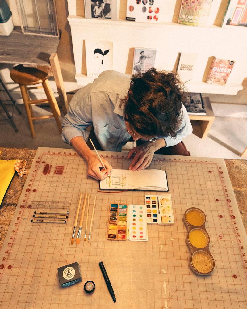 watercolor artist sitting at table with notebook