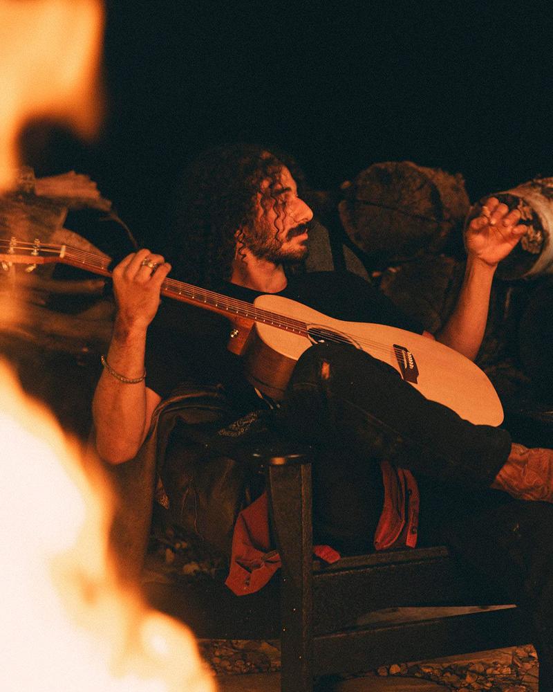 man sitting fireside playing guitar
