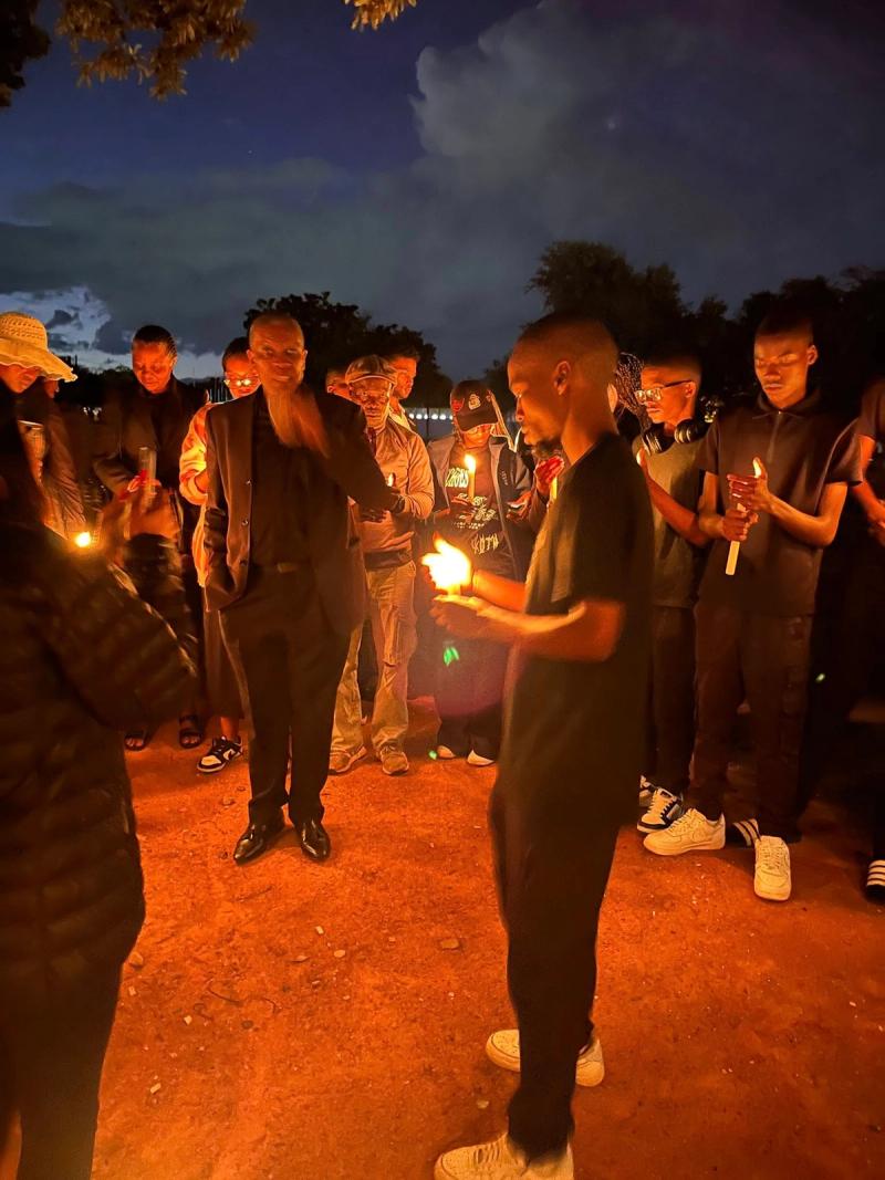 A young man cups a candle flame as mourners stand in a circle at the vigil.