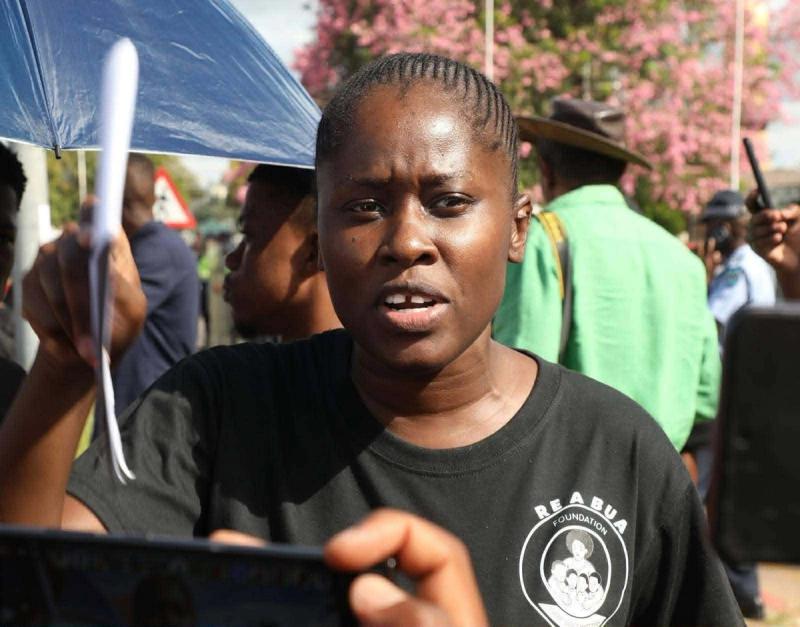 A demonstrator holds an 'End gender based violence' placard with a handprint.