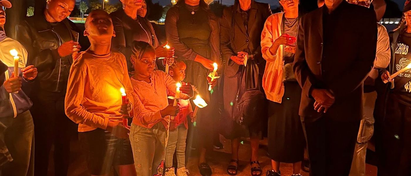 At dusk, a crowd including young children holds lit candles at a Candlelight Justice vigil.