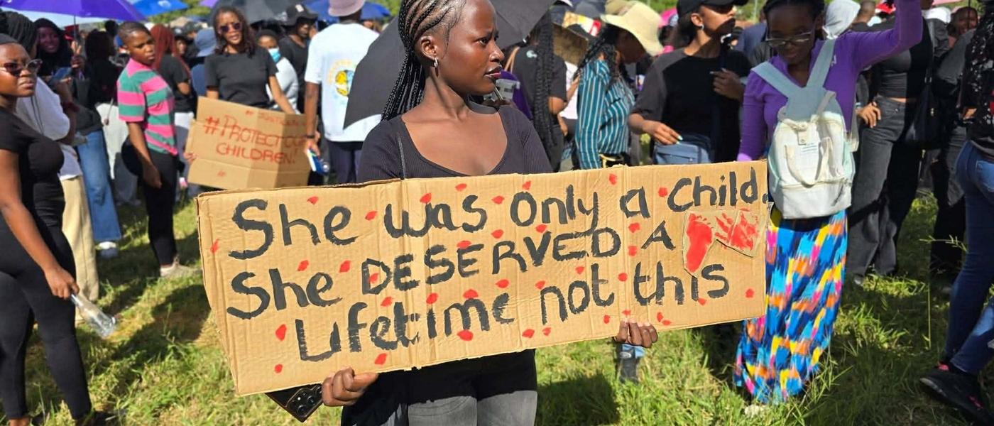 A protester at the march holds a cardboard placard reading 'She was only a child. She deserved a lifetime, not this.'
