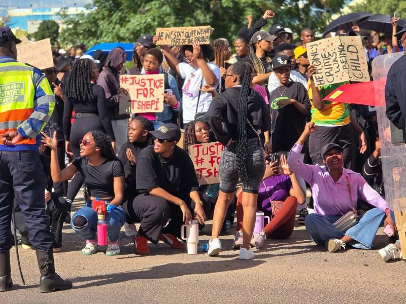 Protesters seated on the road with #JusticeForTshepi signs as police stand by.