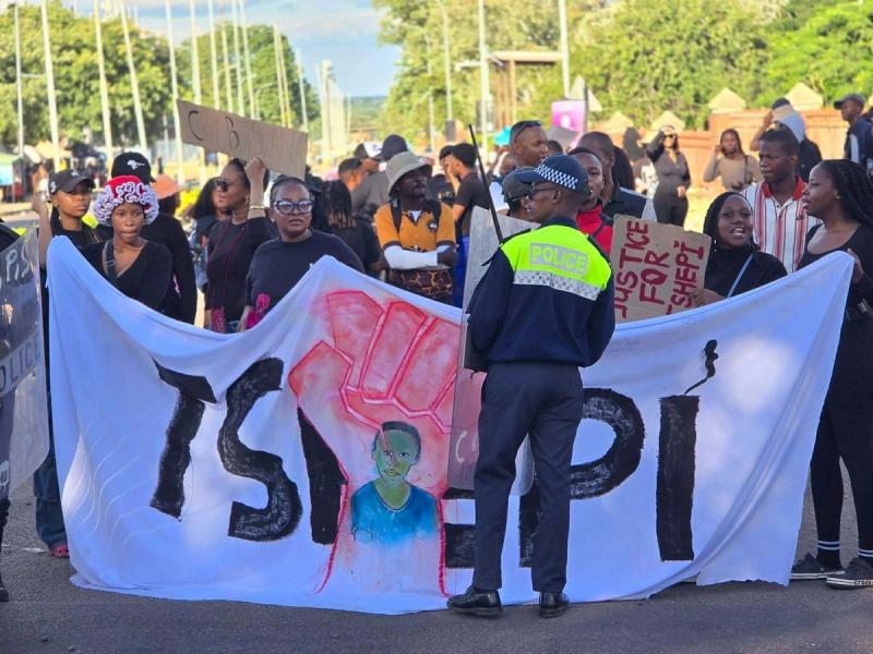 Demonstrators hold a large white banner reading 'TSHEPI' with a raised-fist motif.
