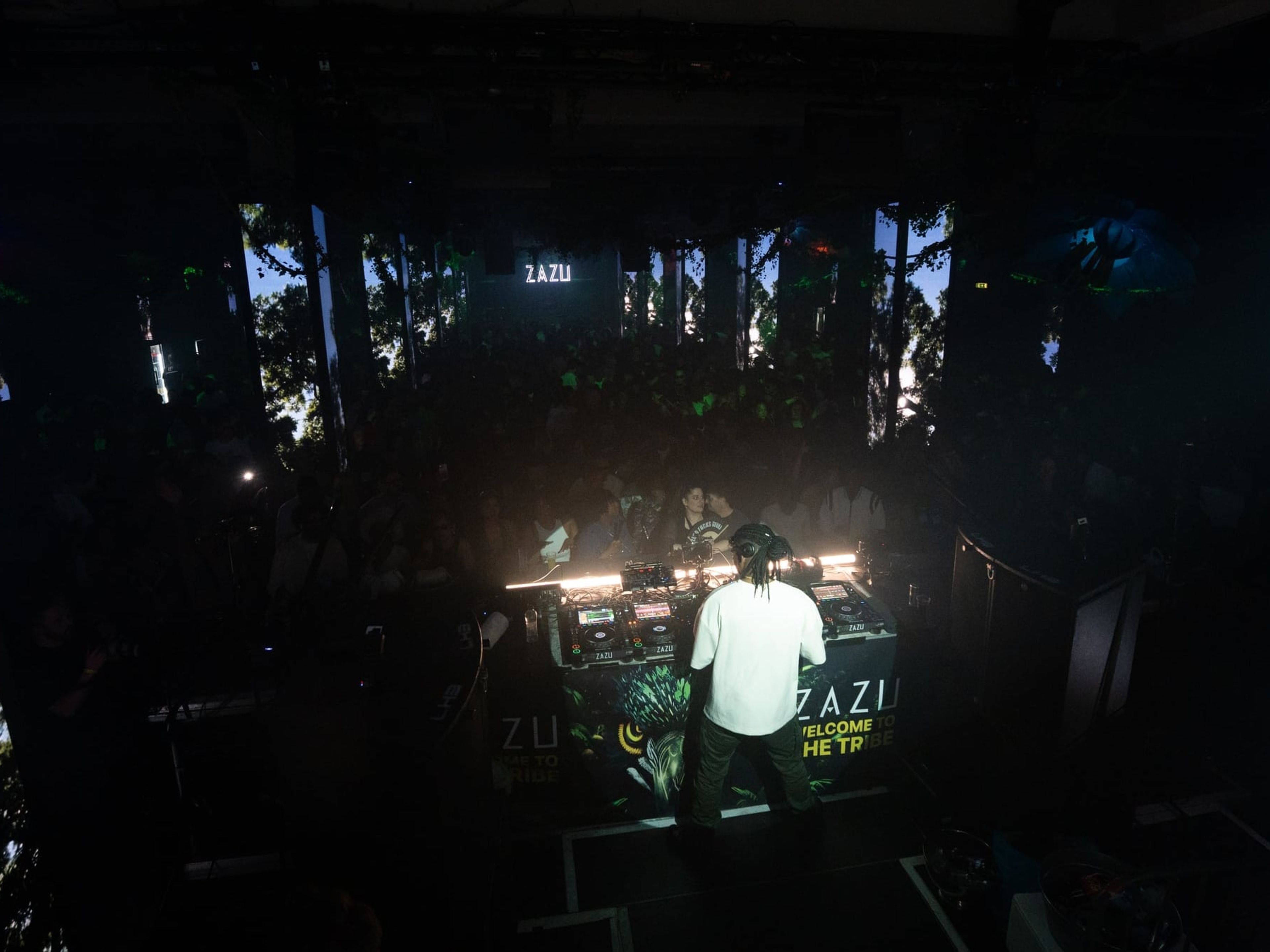 DJ in de booth van Zazu, met publiek en projecties van bomen