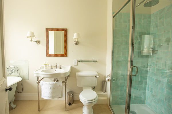 Standard bedroom bathroom with a roll-top bath, glass shower with turquoise tiles, washstand basin and toilet