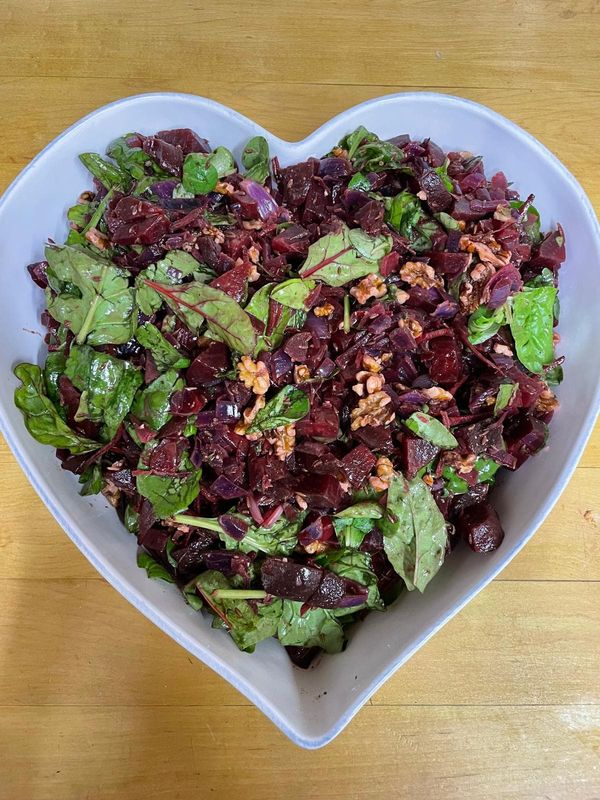 Beetroot salad with spinach and chard leaves, red onion, walnuts and seeds in a heart-shaped white bowl