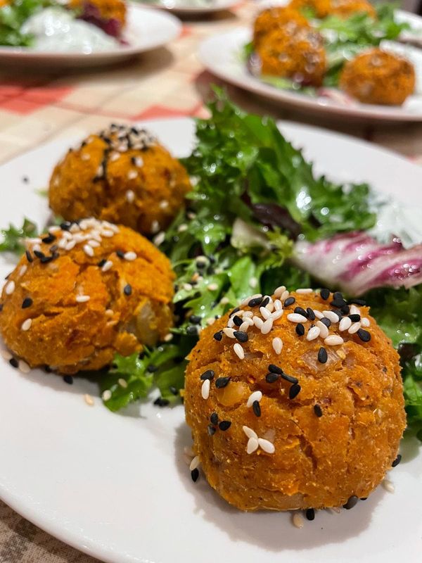 Three orange baked balls topped with black and white sesame seeds, served with a dressed leafy salad on a white plate
