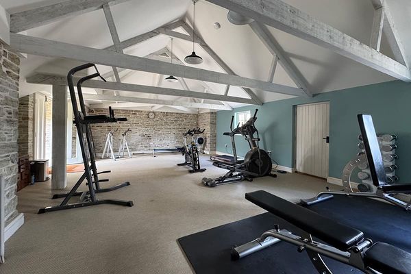 Gym with exercise bike, cross trainer, weights bench and dumbbells under painted timber beams, with stone and teal walls