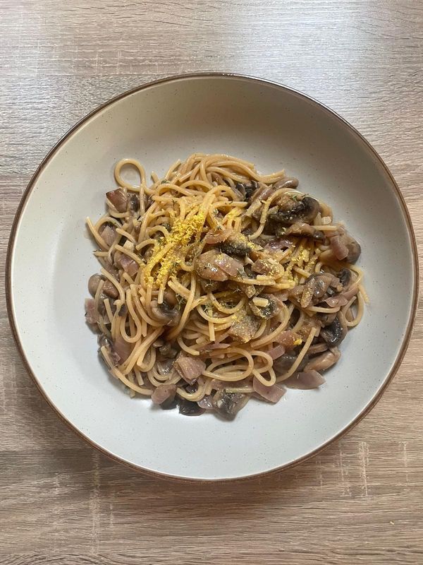 Spaghetti with mushrooms, red onion and thyme, finished with a fine yellow grated topping, in a speckled bowl