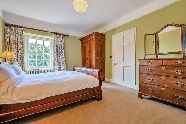 Deluxe bedroom with a wooden sleigh bed, wardrobe and chest of drawers, green walls and a sash window overlooking trees
