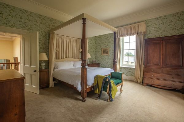 Deluxe bedroom with a wooden four-poster bed, green velvet bench, large wardrobe and green floral wallpaper