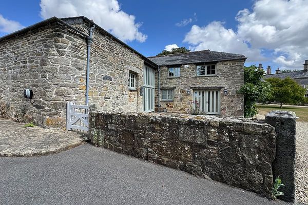 Stone building with a slate roof and sage green doors and windows, behind a low stone wall and white gate