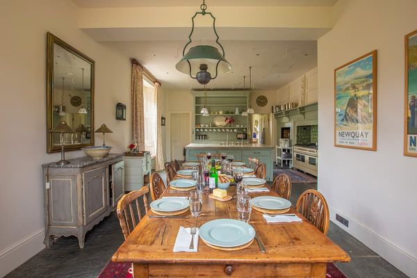 Long wooden dining table laid with pale blue plates, opening onto a farmhouse kitchen with a green dresser and range cooker