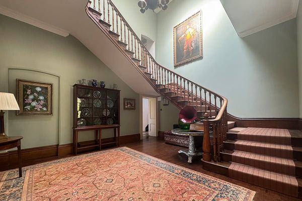 Entrance hall with a sweeping wooden staircase, sage green walls, a large patterned rug, display cabinet and gramophone