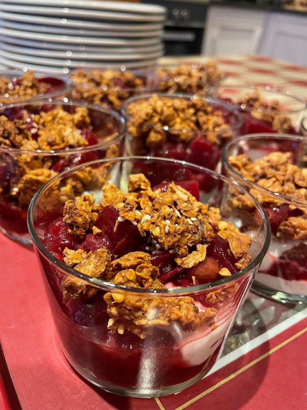 Glass pots layered with white yoghurt and red fruit compote, topped with crunchy granola and sesame seeds
