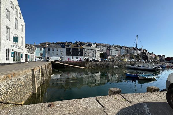 Mevagissey harbour with small boats on still water and a row of colourful stone houses climbing the hillside behind