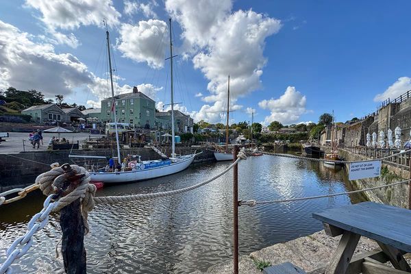 Tall ships moored in Charlestown harbour beside a green harbourside inn, with ropes and a picnic bench in the foreground