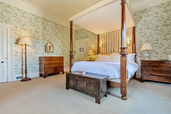 Deluxe bedroom with a wooden four-poster bed, chest at its foot, two chests of drawers and green floral wallpaper