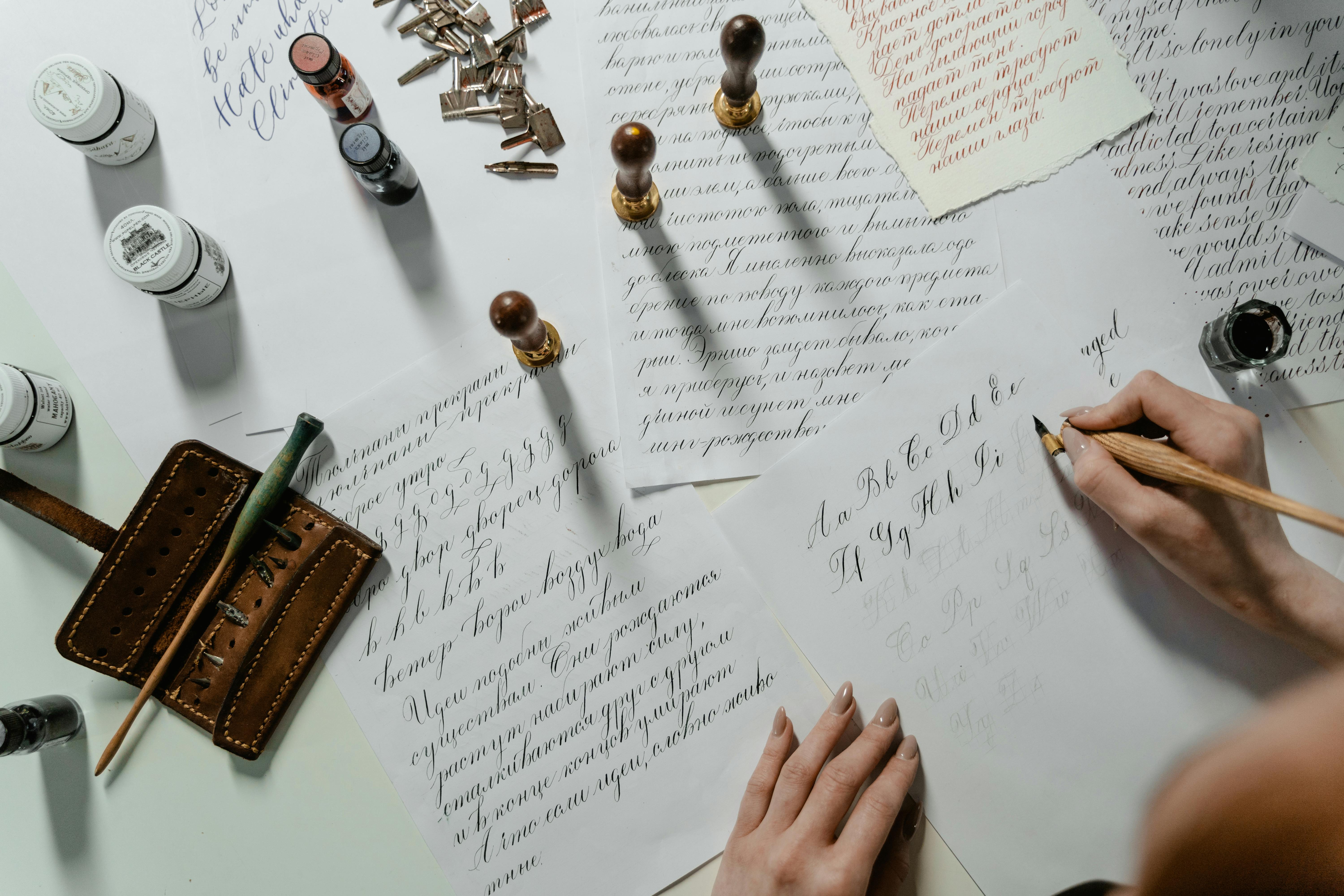 A ladies hands holding a quill, writing on a page, many previously written pages in the background.