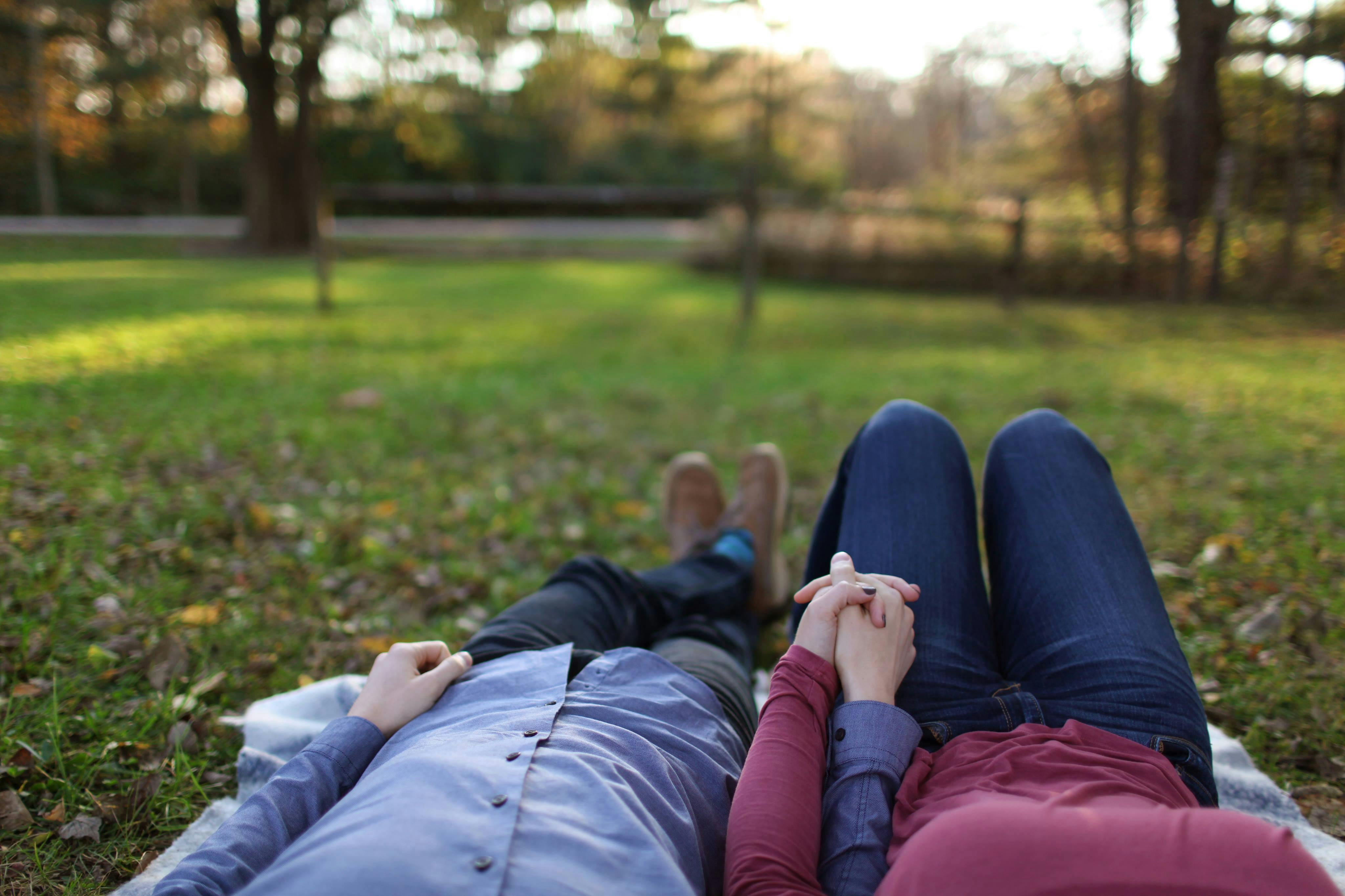 Couple laying in the grass holding hands on a picnic blanket