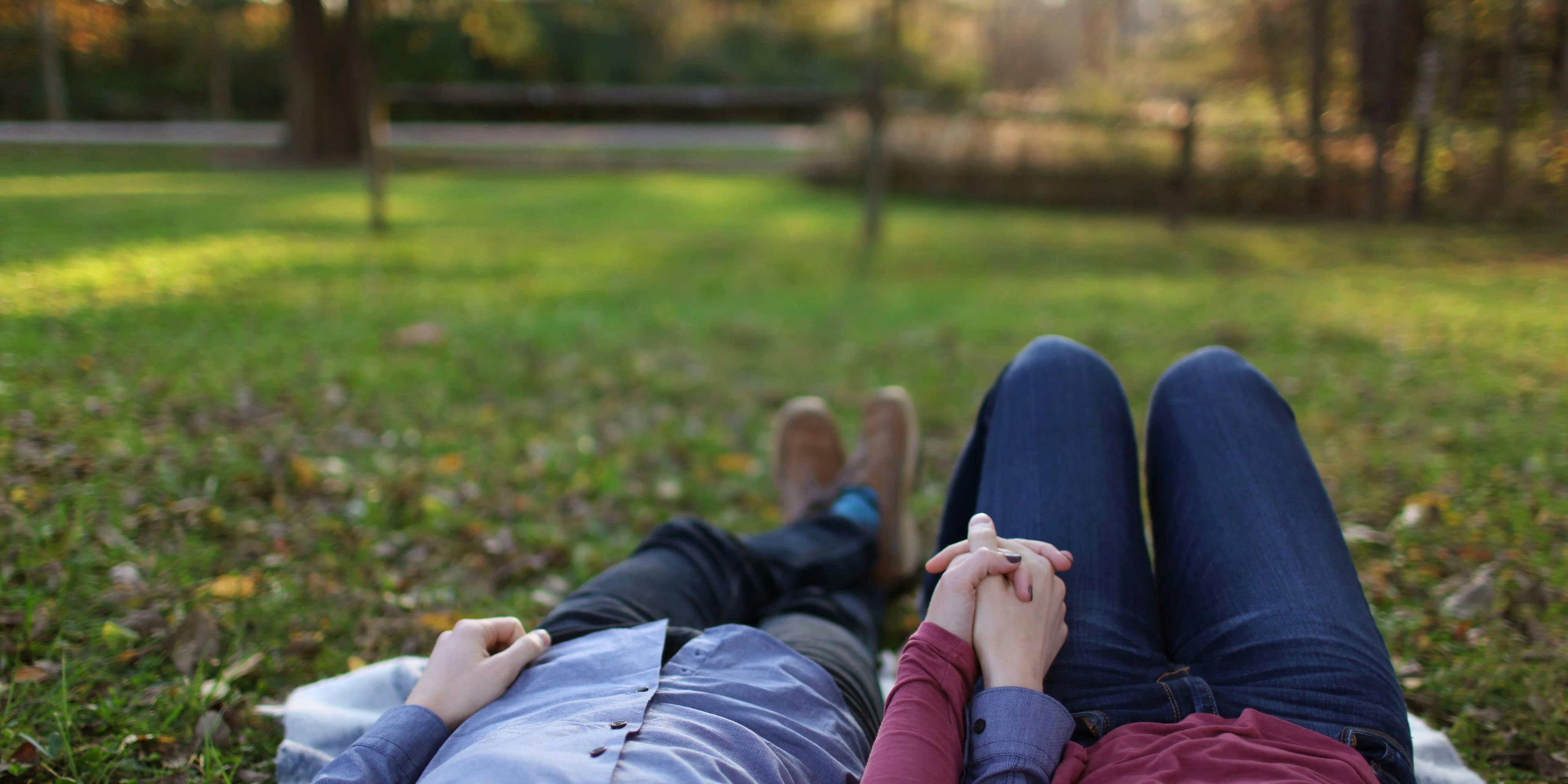 Couple laying in the grass holding hands on a picnic blanket