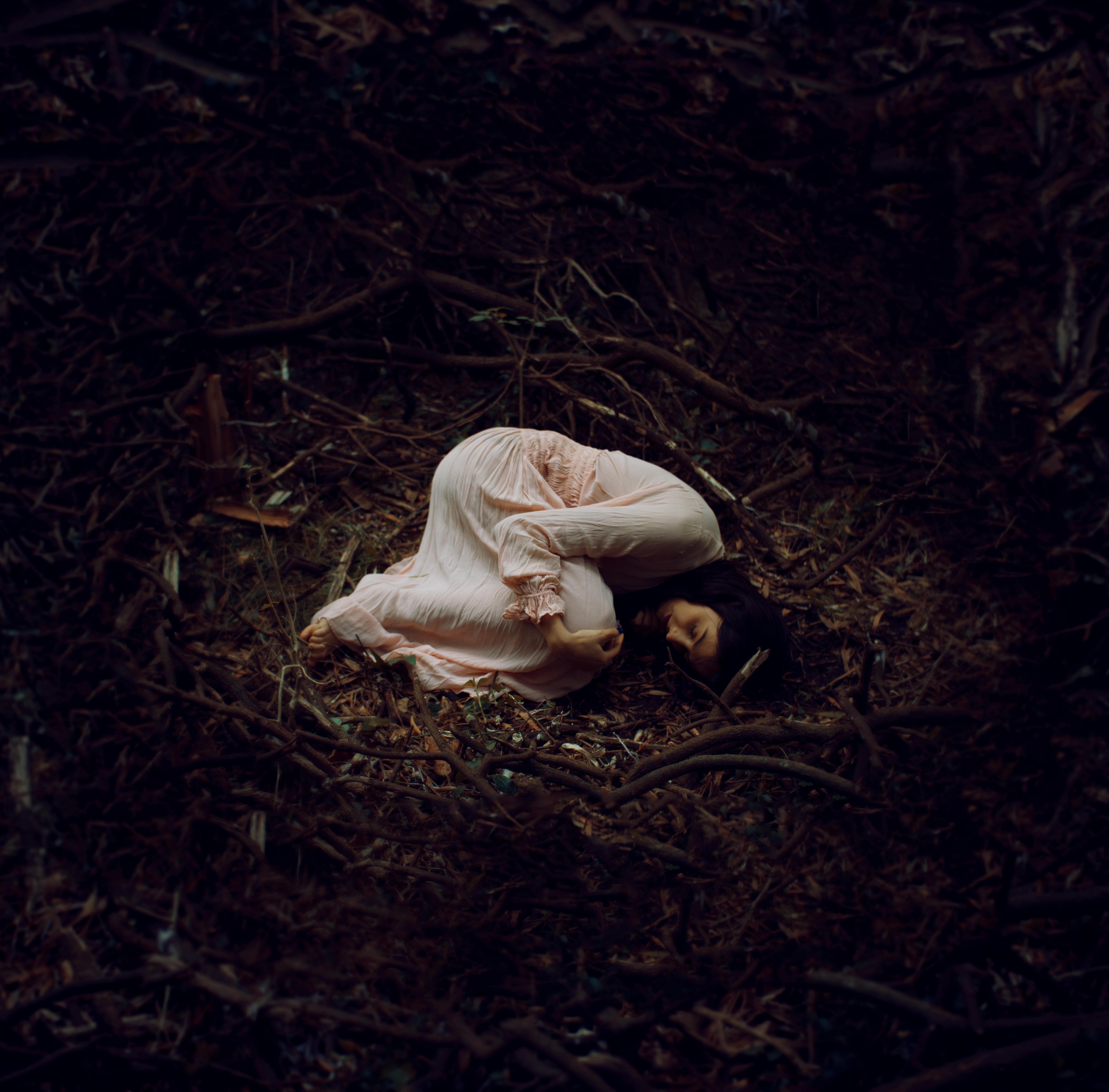 Women in a white dress laying in the fetal position in a field alone.
