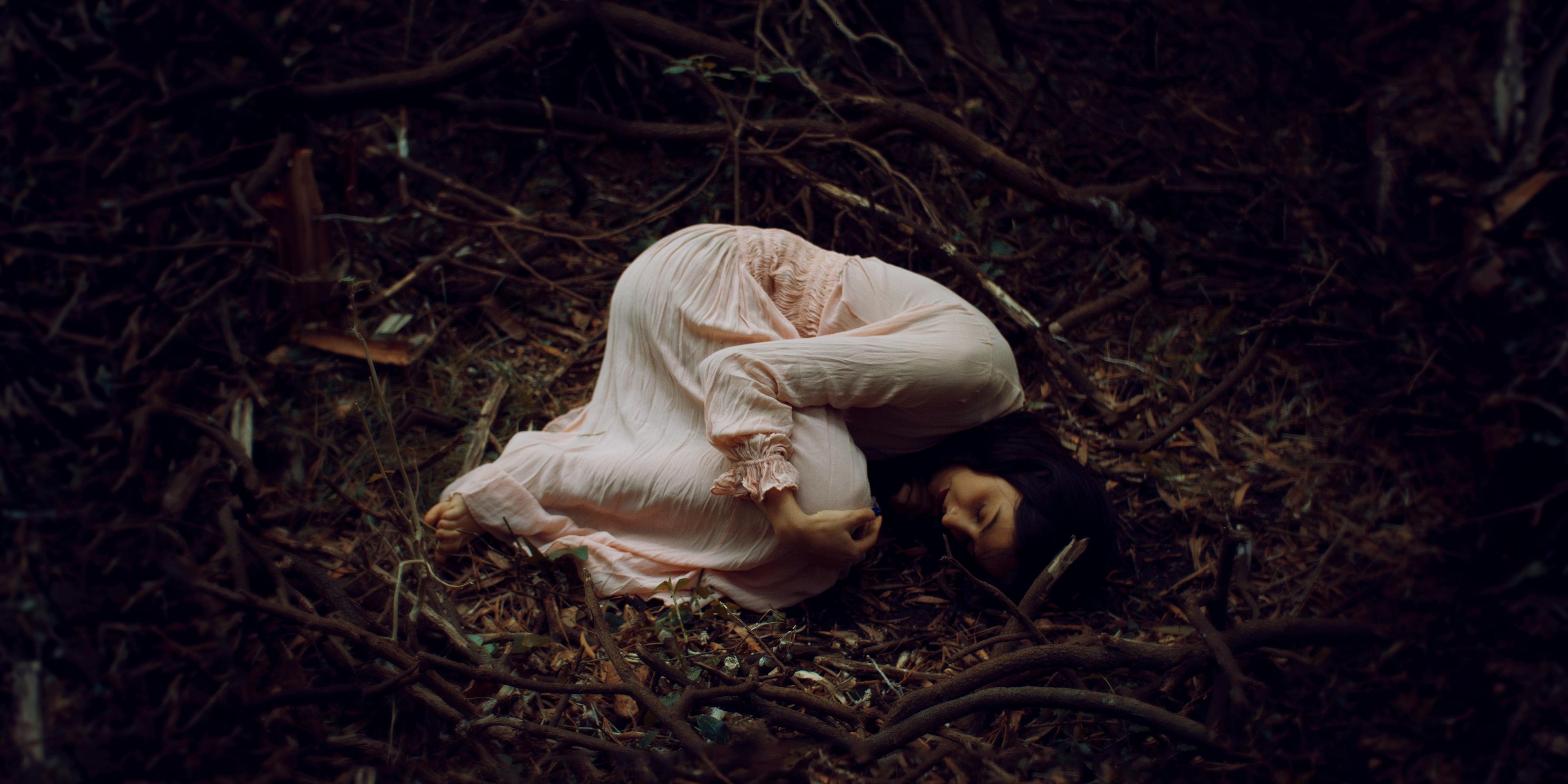 Women in a white dress laying in the fetal position in a field alone.
