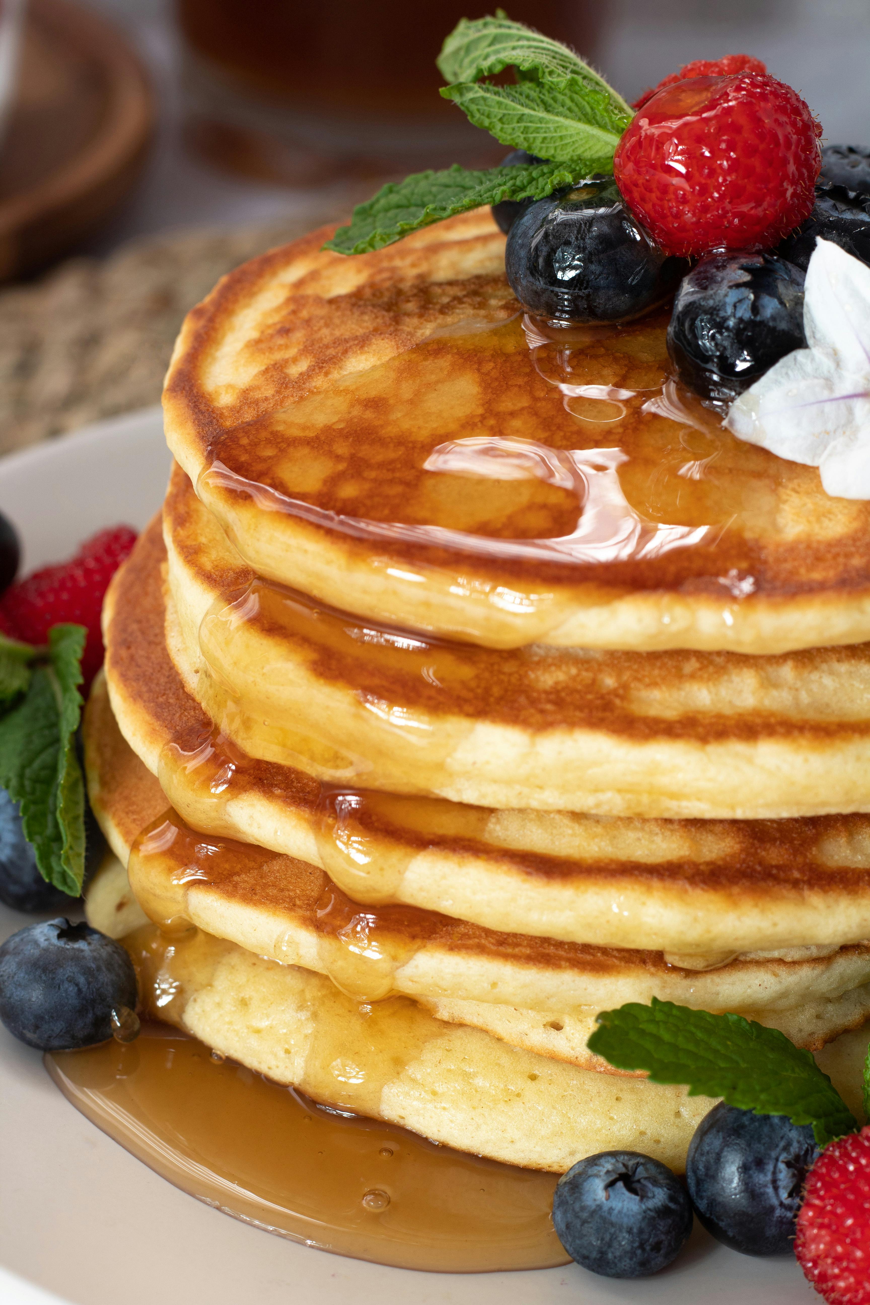 Stack of flapjack pancakes with berries on top and sides, syrup dripping down the stack