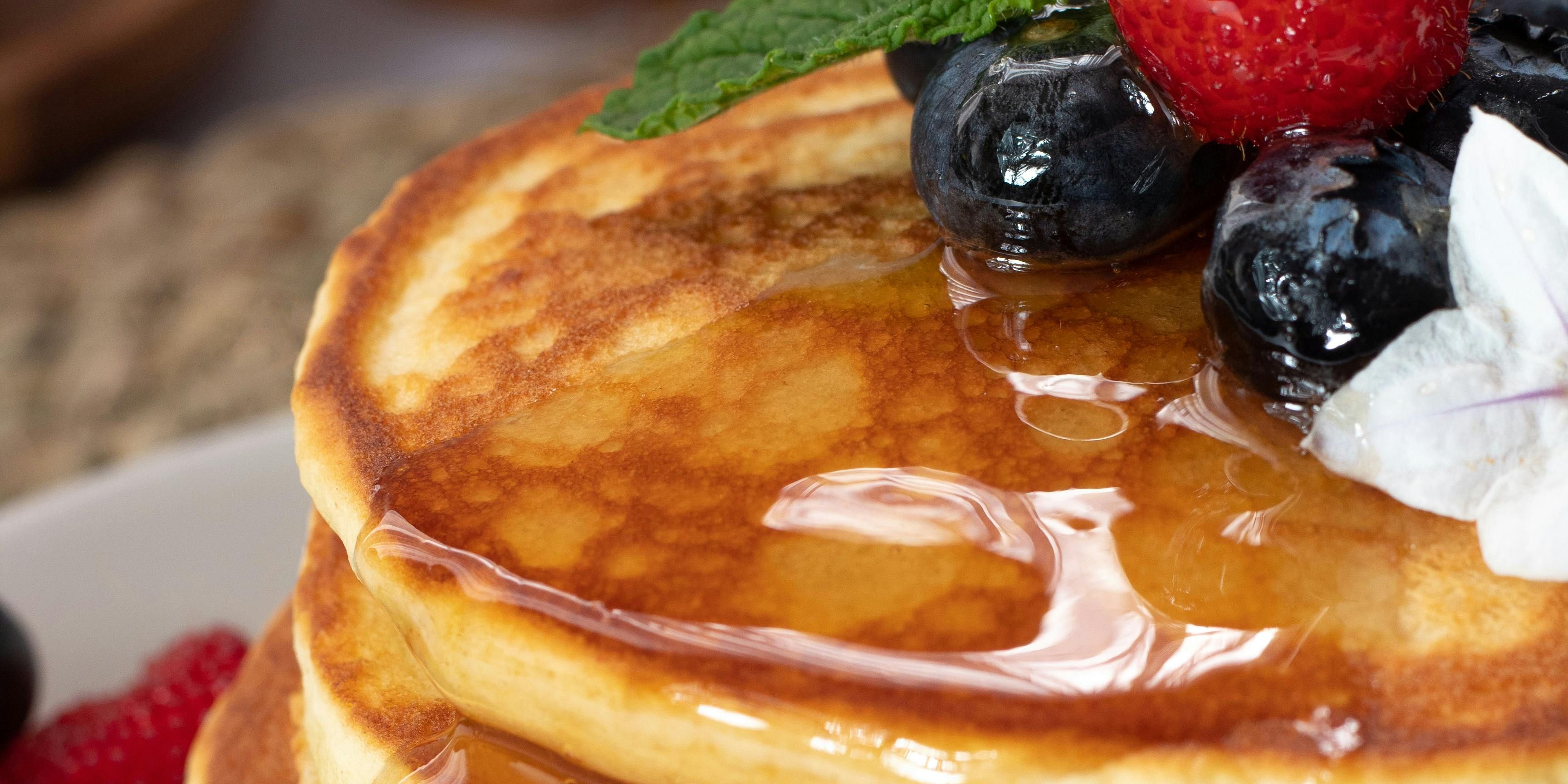 Stack of flapjack pancakes with berries on top and sides, syrup dripping down the stack