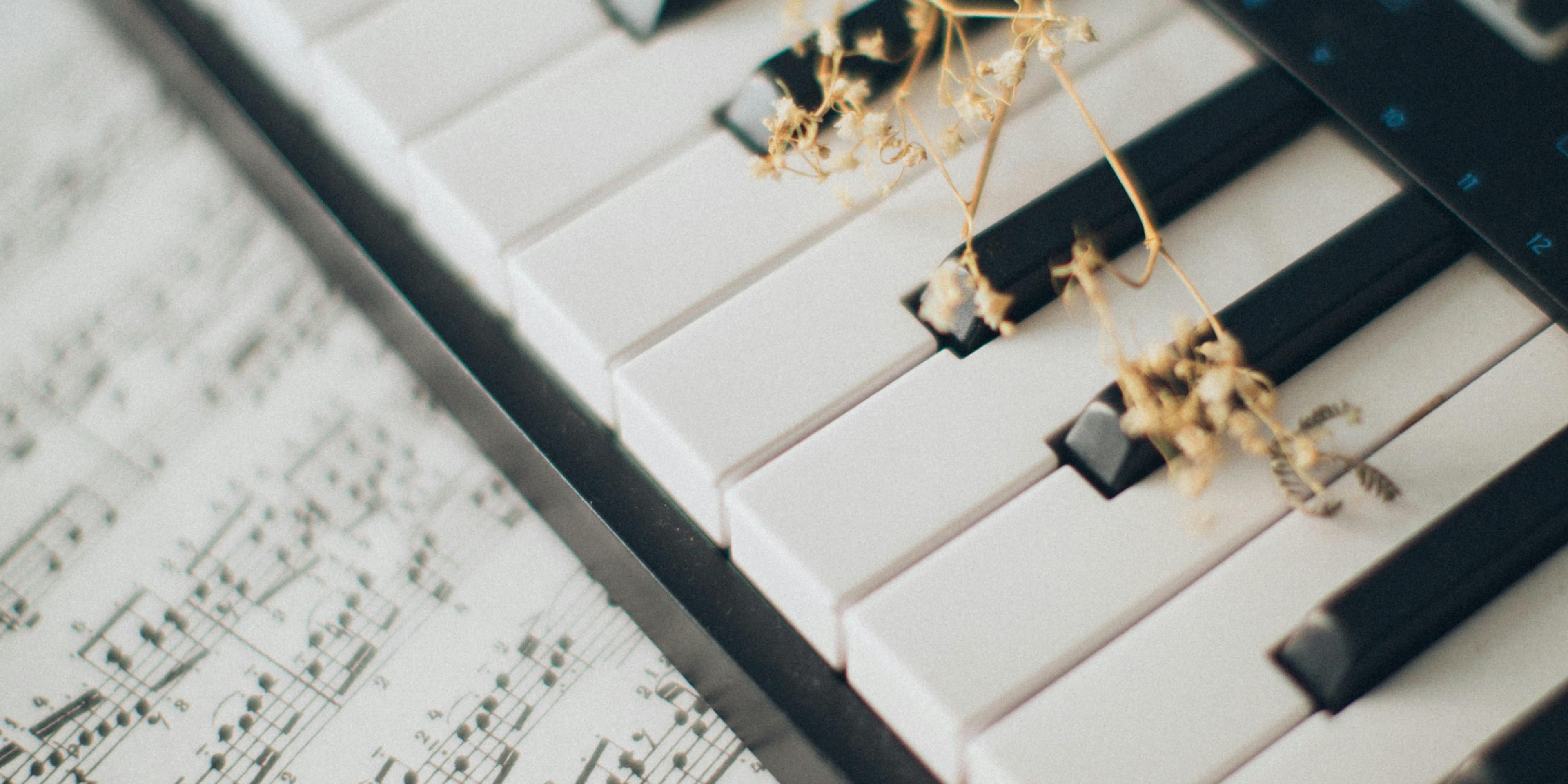 Piano keyboard with sheet music underneath and a golden branch laid across the keyboard