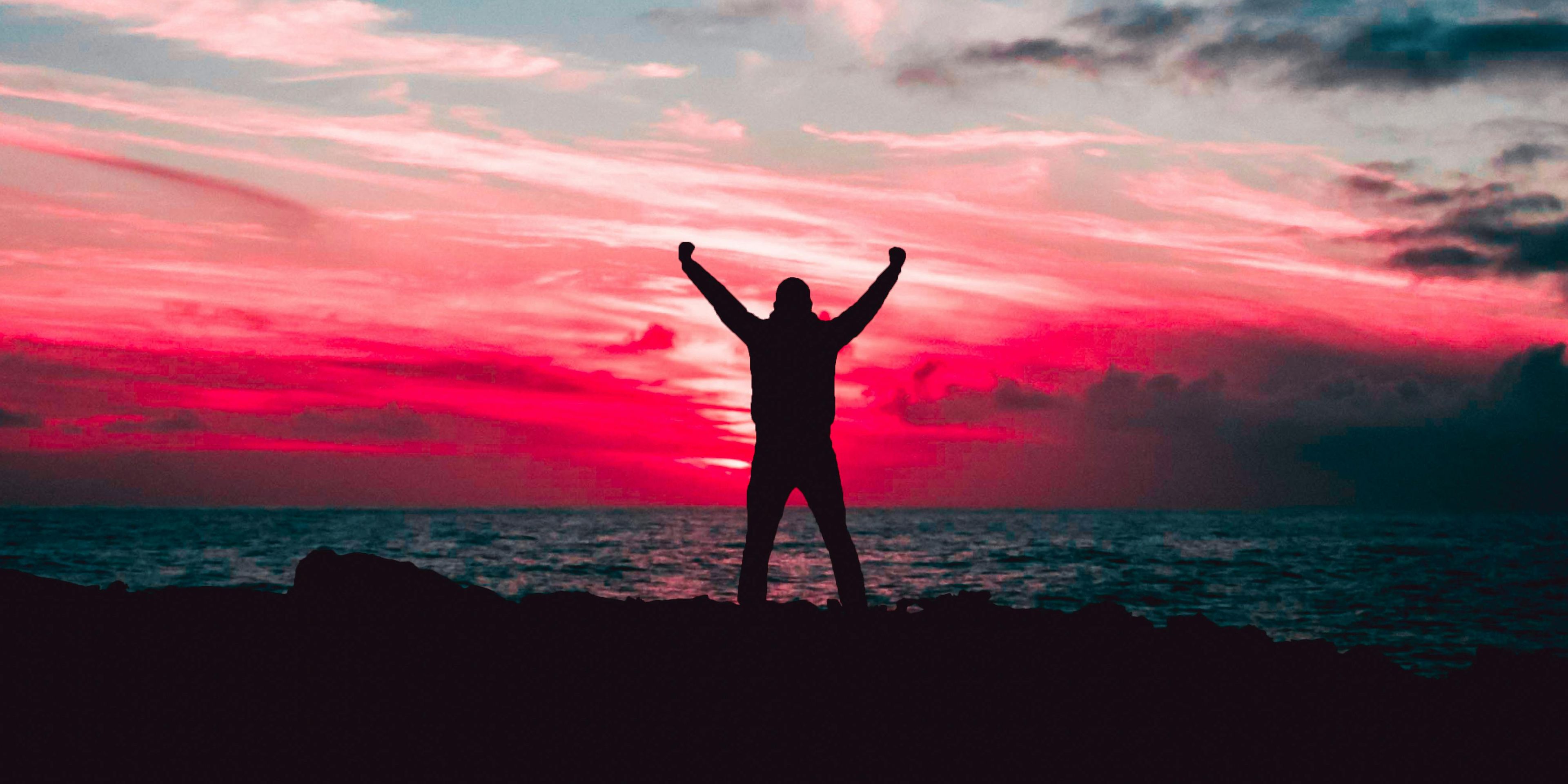 Person standing in front of a colorful sky celebrating
