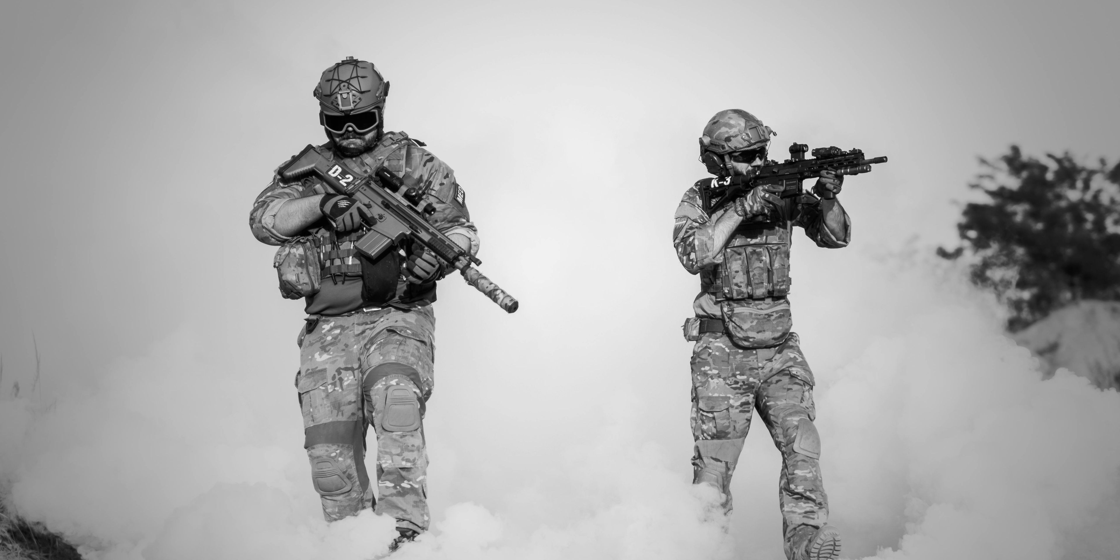 Two soldiers in camouflage tactical gear holding guns and walking through smoke grenades