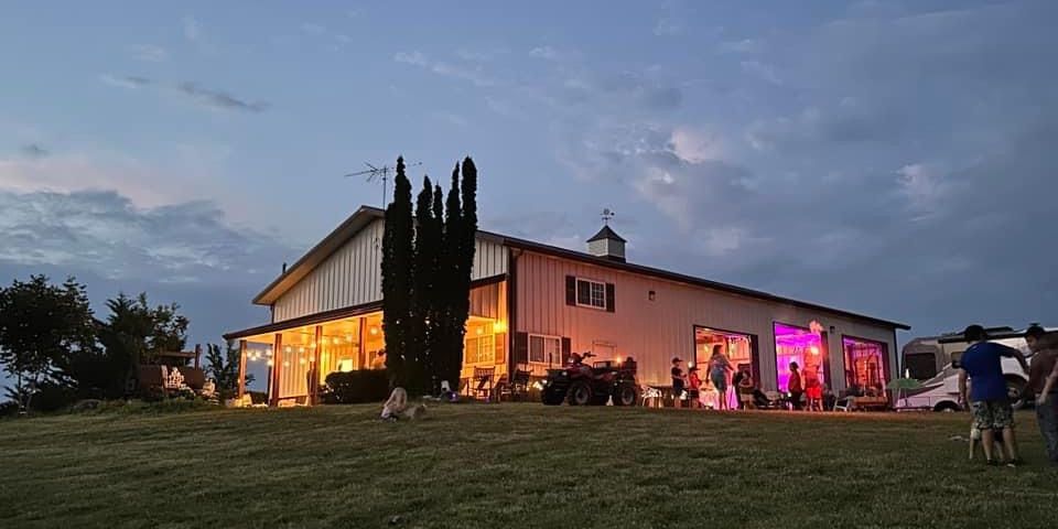 Farm barn with colorful lights emanating out of the garage doors, kids playing, people celerating
