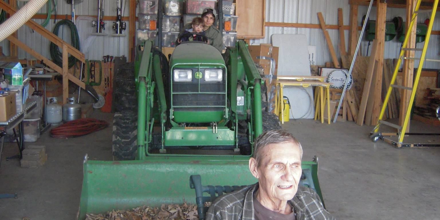 Two kids playing on a tractor in their grandpas workshop. Grandfather sitting enjoying the presence of his grandchildren