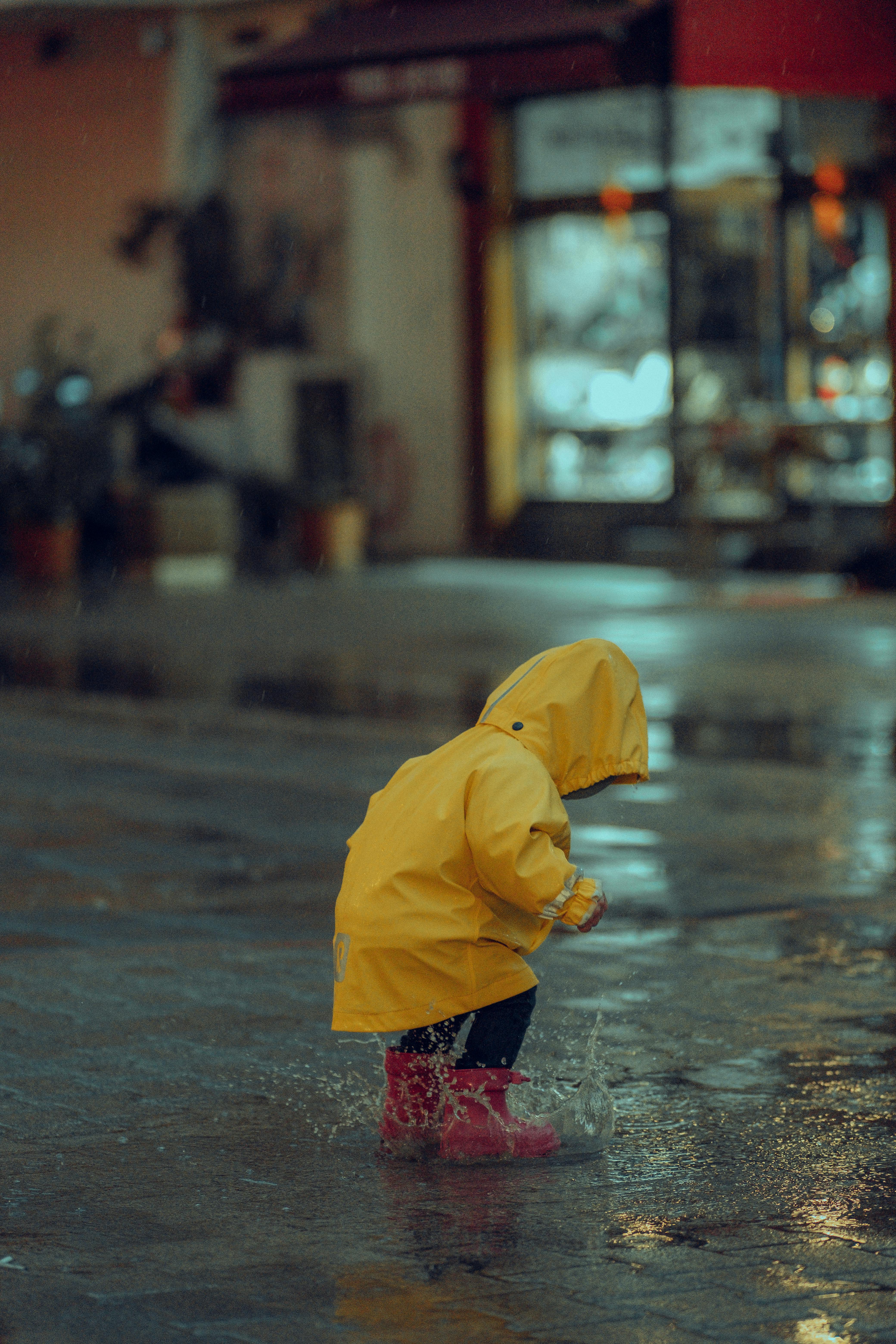 Child splashing in puddles playing in the rain on an empty street