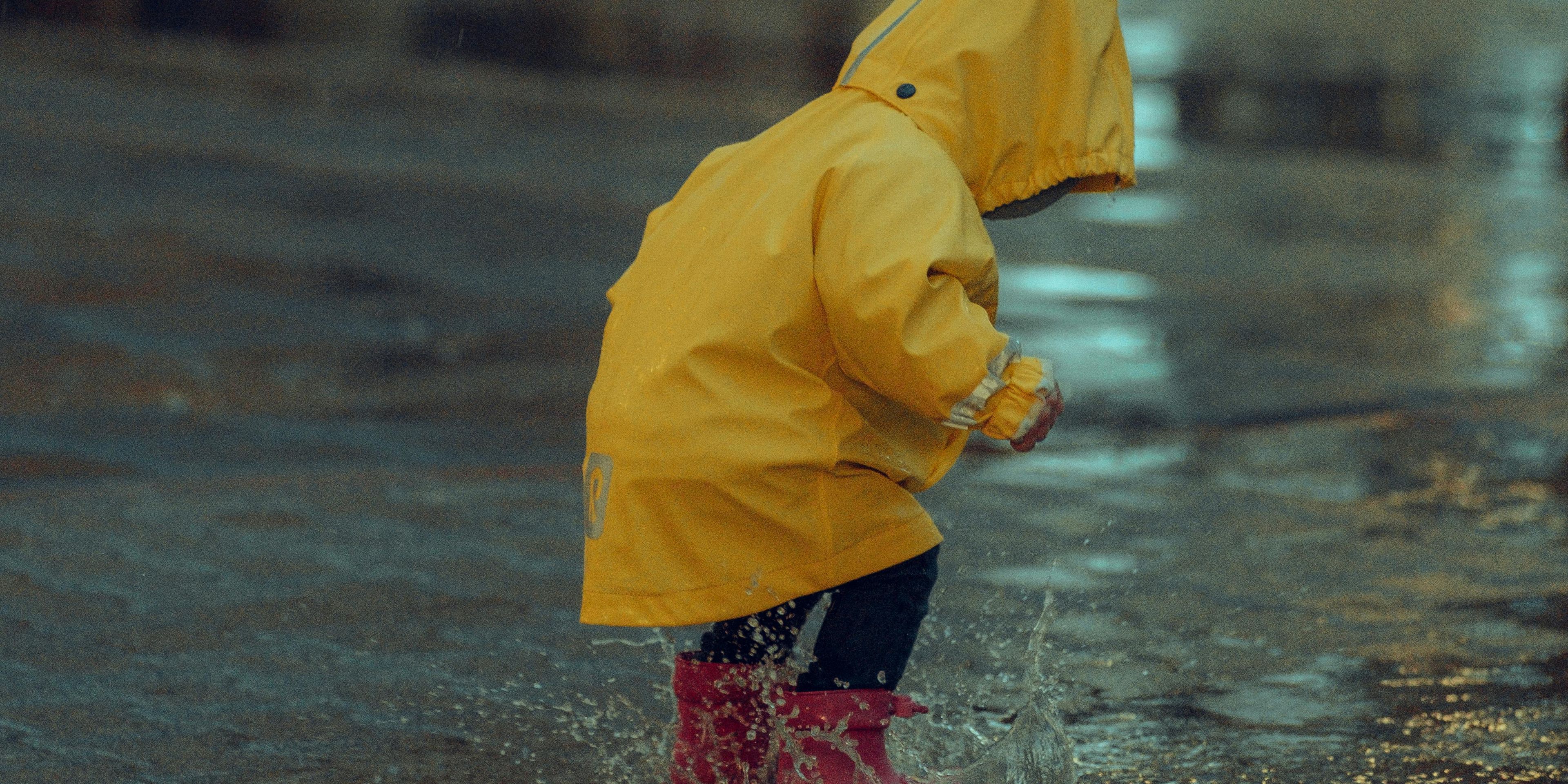 Child splashing in puddles playing in the rain on an empty street