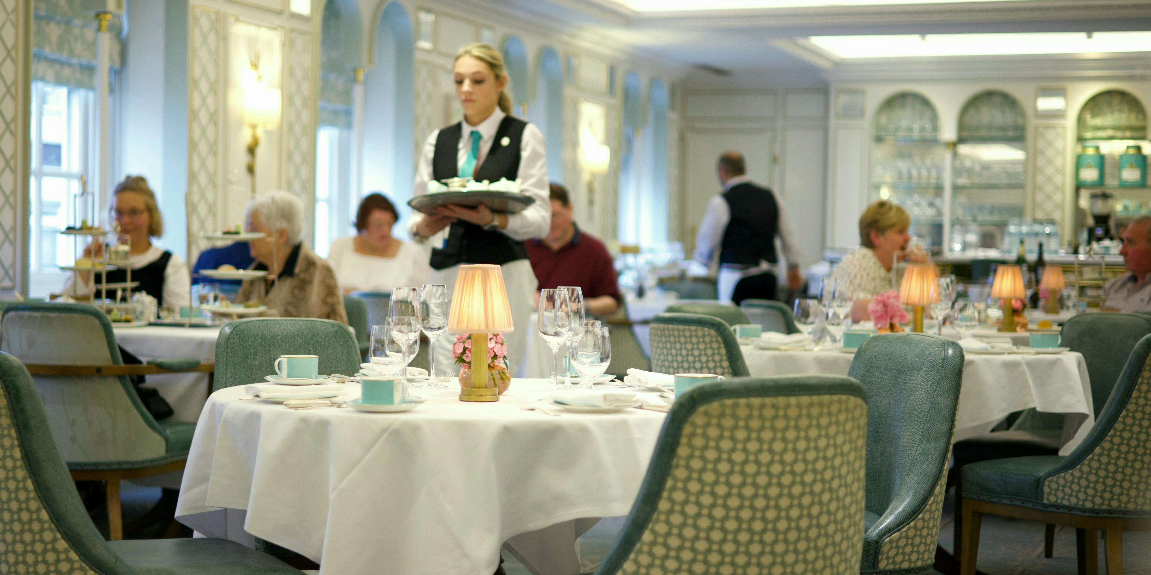 Restaurant with set table in foreground, tables with diners and waitstaff actively attending them.
