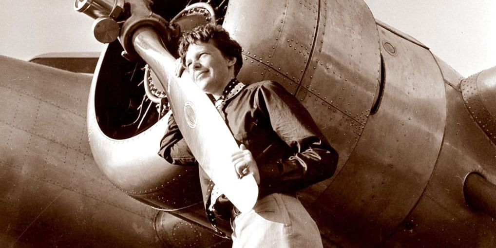 Amelia Earhart holding on the propeller of a plane