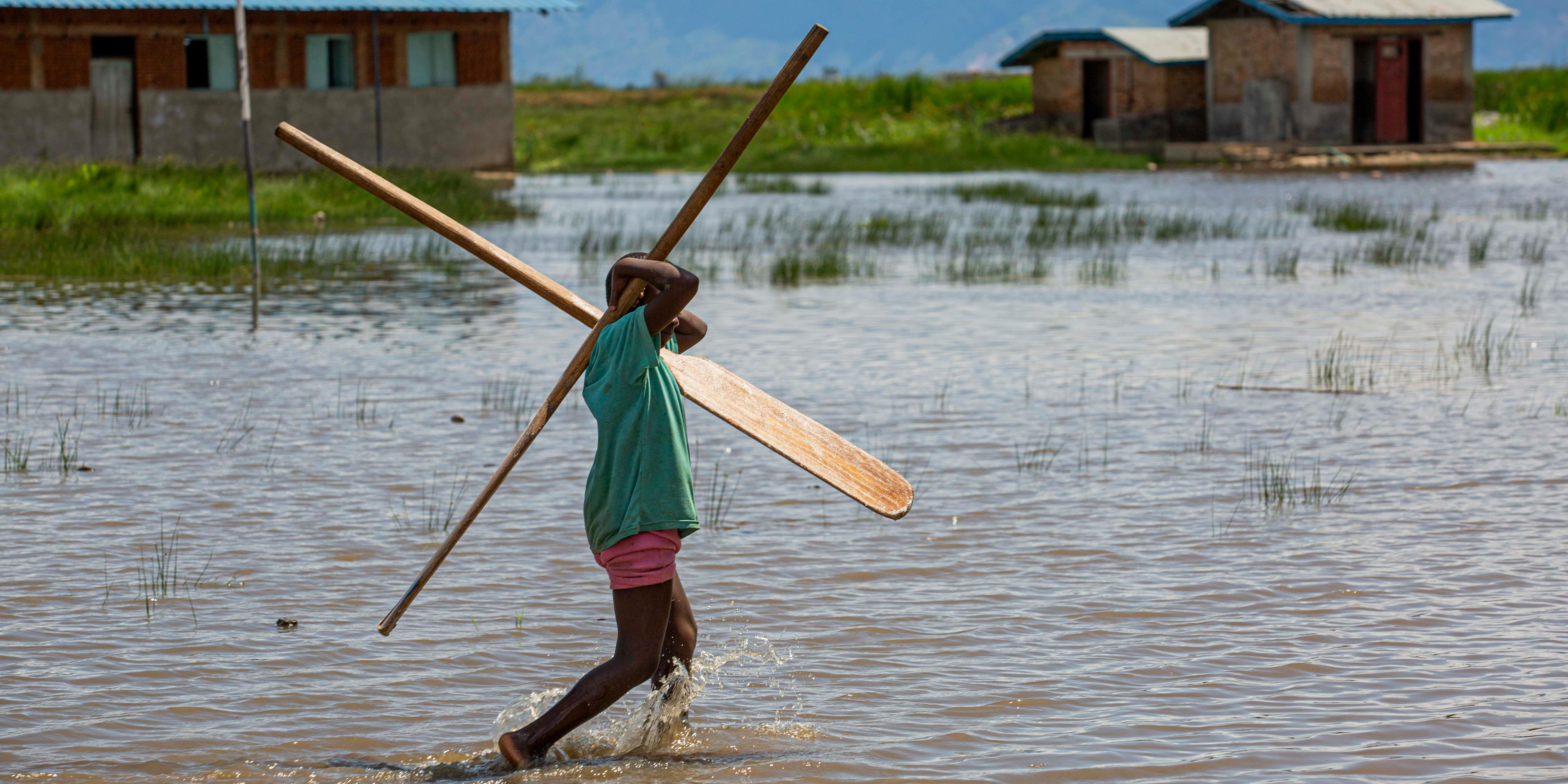 Man wading through flood waters, carrying two paddles on his shoulders forming a cross.
