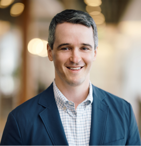 A man in a blue jacket and plaid shirt smiles for the camera