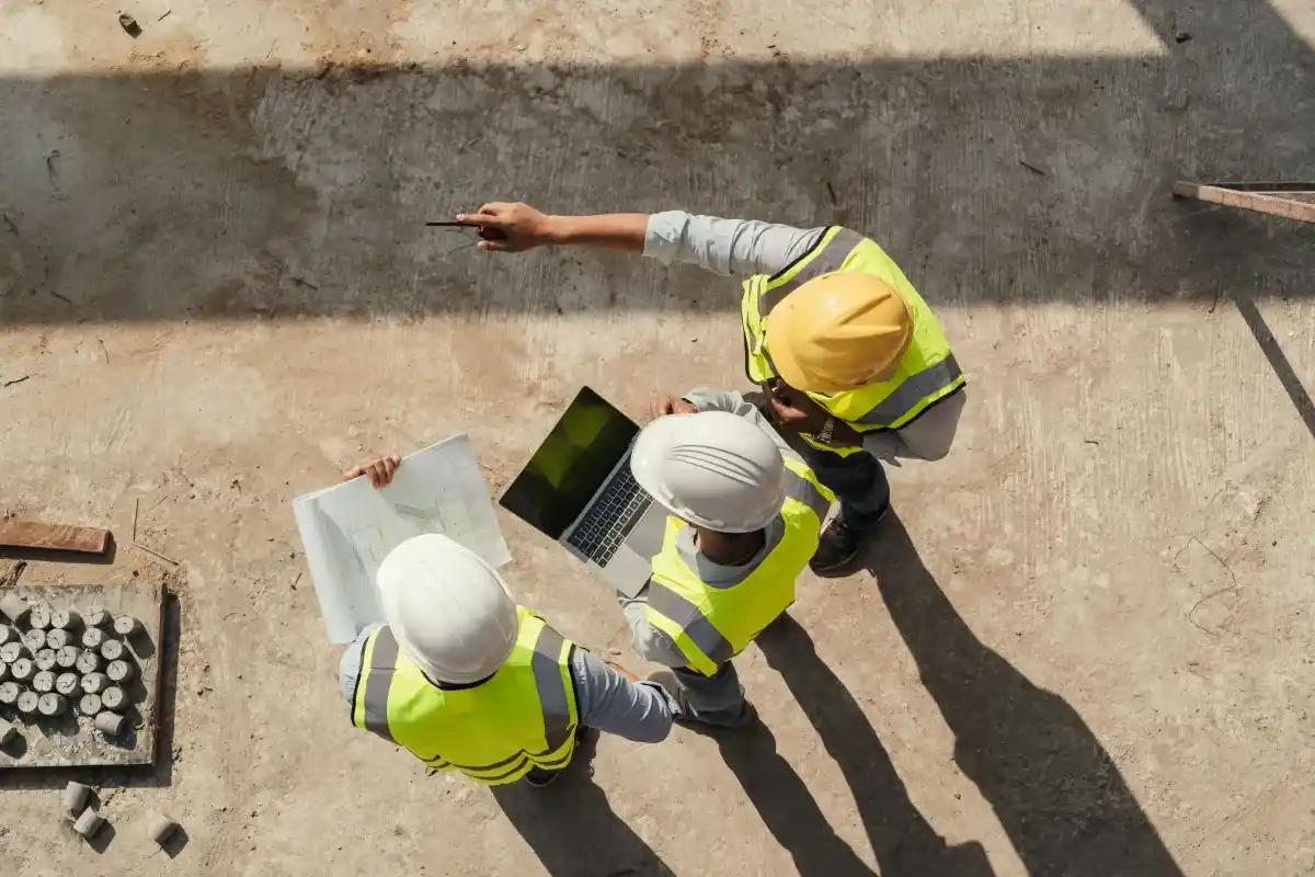A group of construction workers are looking at a laptop on a construction site