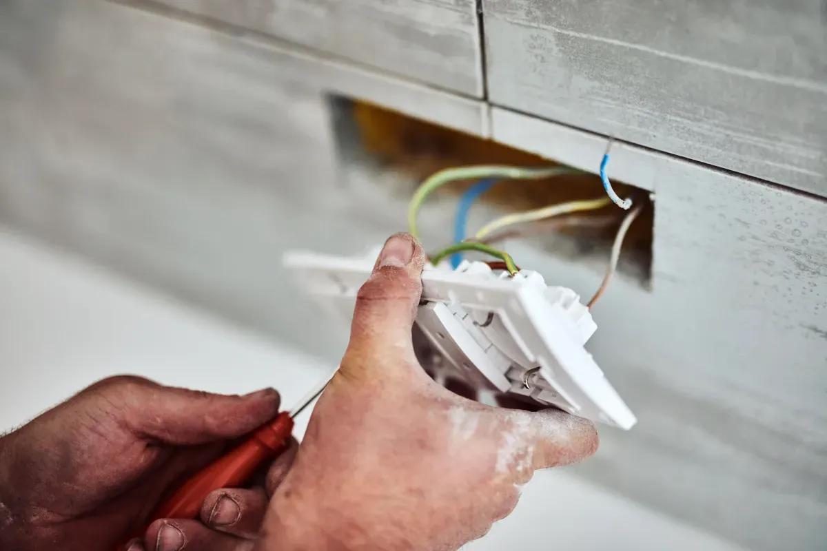 A man is fixing an electrical outlet with a screwdriver